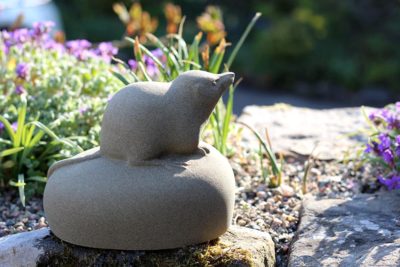Jennifer Tetlow: This beautiful stone carving, sculpture by Jennifer Tetlow represents a small shrew. It is perched on a little mound, with its nose lifted inquisitively. Each piece of Jennifer Tetlow sculpture is individually carverd from York stone and exhibited at Norton Way Gallery Hertfordshire. This piece is shown at home in a sunny garden.