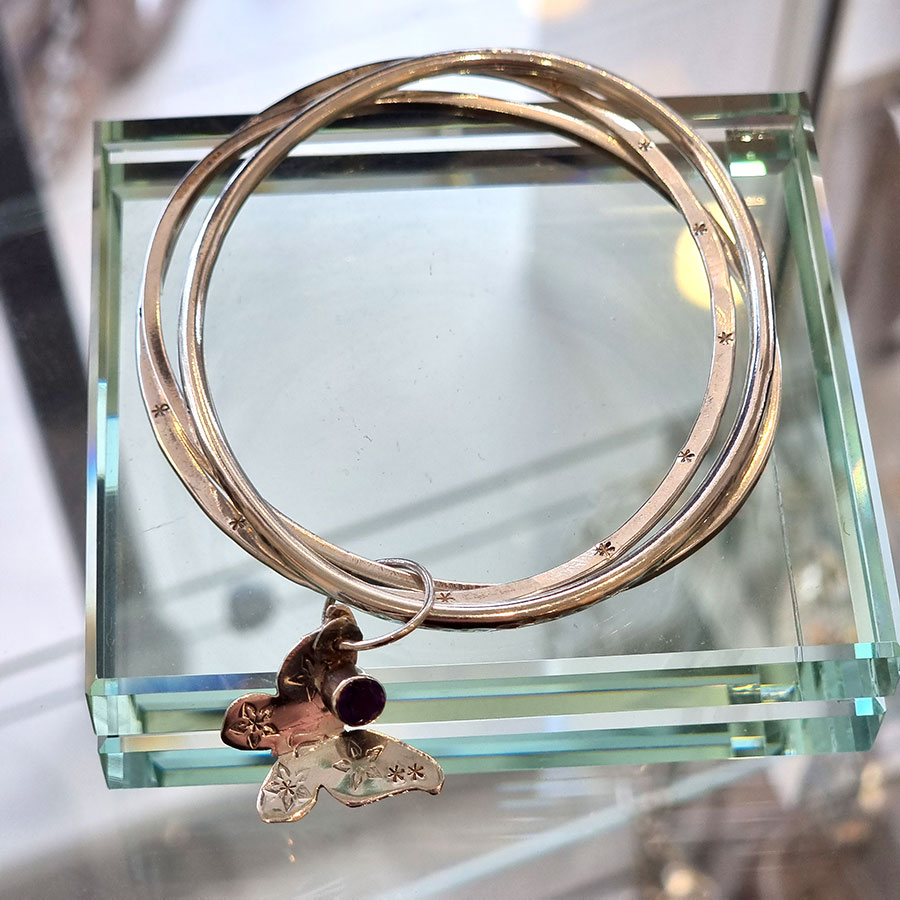 Lou Shotter at Norton Way Gallery, Hertfordshire. This original artwork by British artist, Lou Shotter is created in Stirling Silver and Amethyst. It is a beautiful group of three slim bangles, collected by a silver ring with a butterfly and Amethyst. A piece of jewellery.